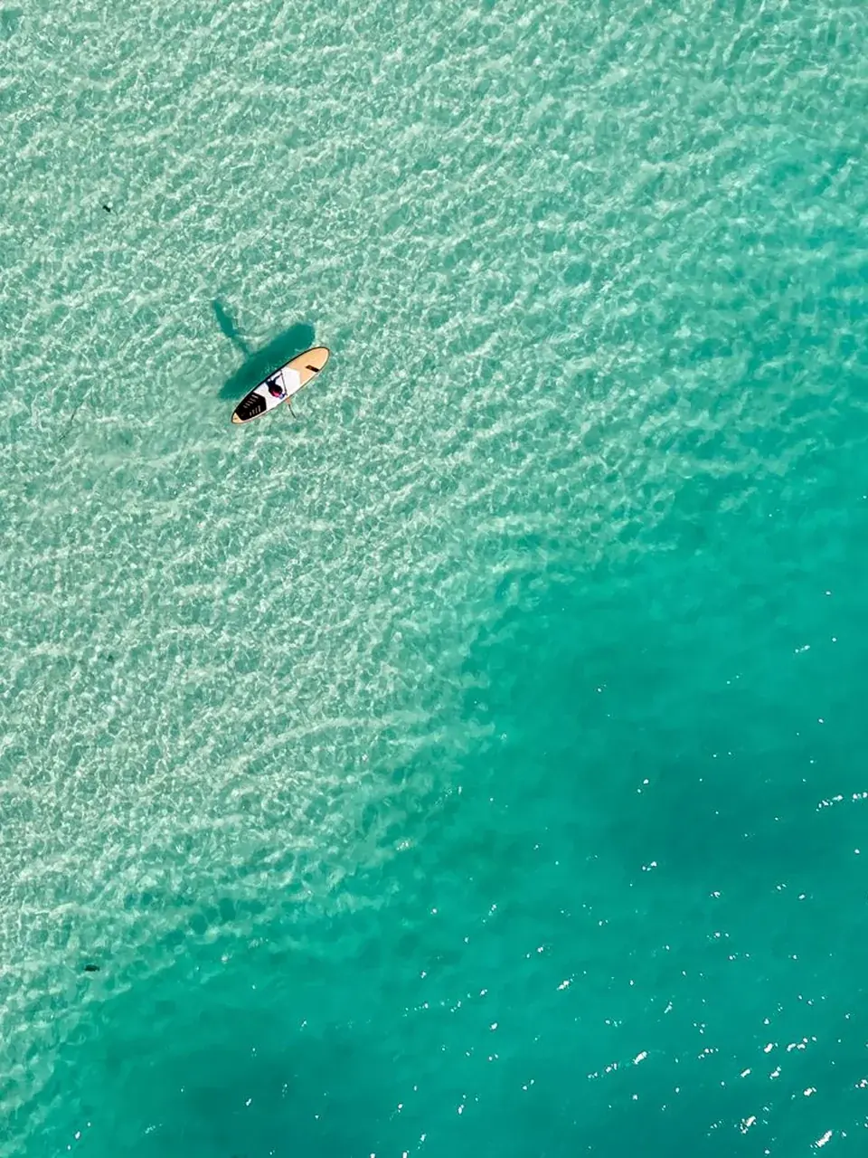 Solo paddleboarder traveling over clear turquoise water