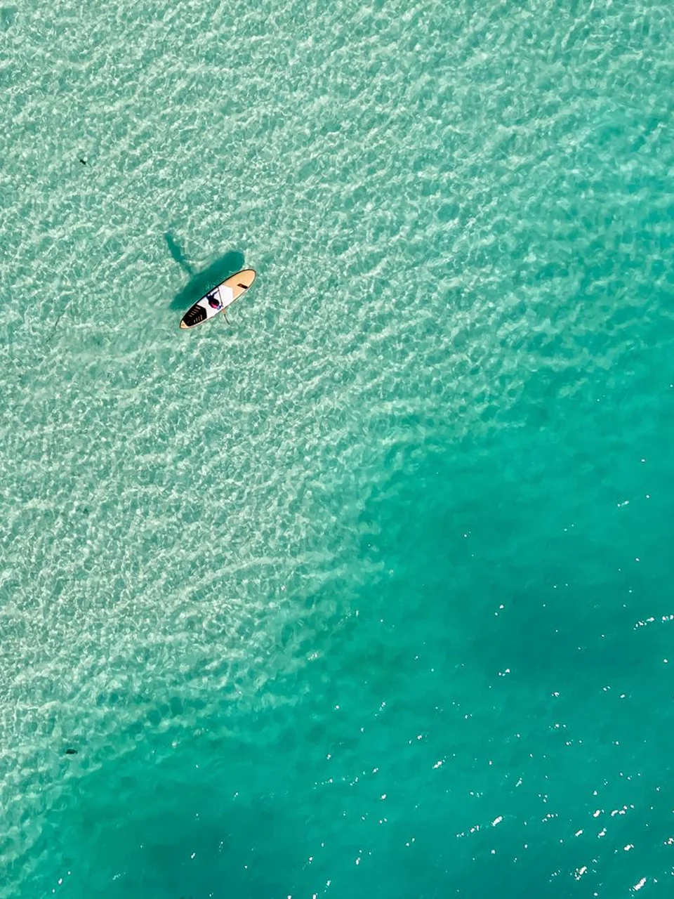 Solo paddleboarder traveling over clear turquoise water
